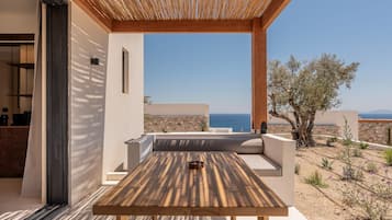 An outdoor seating area with a table and cushions, overlooking a coastal landscape.