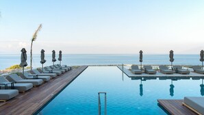 A poolside area with lounge chairs and umbrellas, overlooking a calm sea. - Koia All-suite Wellbeing Resort (Kos)