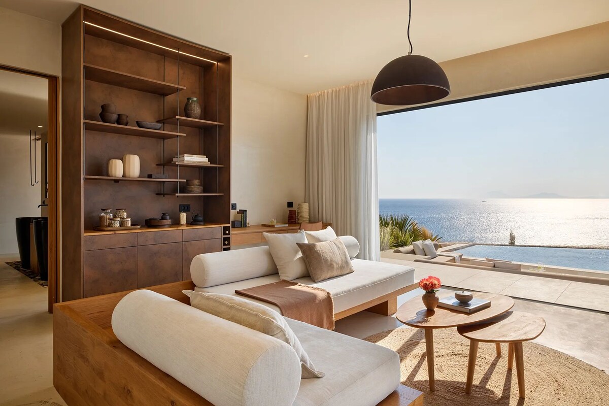 Ein modernes Wohnzimmer mit einer Couch, einem Holzregal und Blick auf den Ozean.