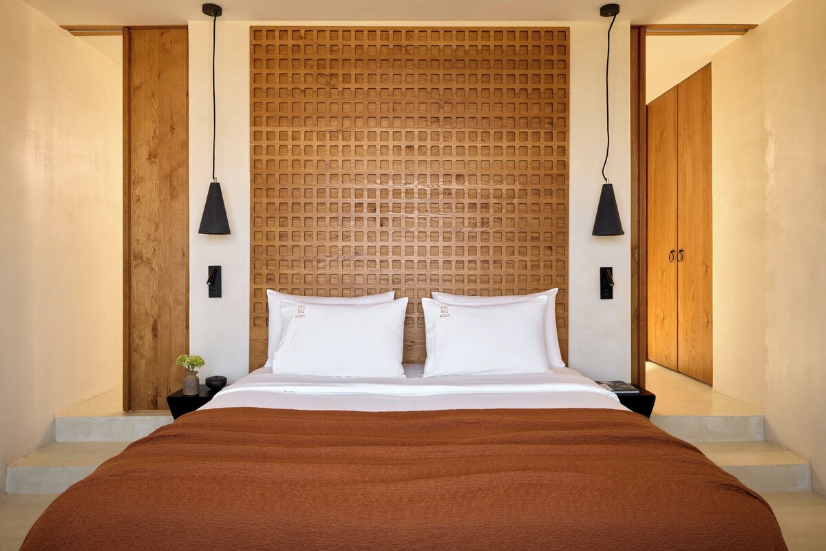 A modern bedroom with a large bed, wooden headboard, and two pendant lights.