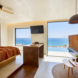 A modern bedroom with a large window, a bed, a desk, and a view of the sea. - Koia All Suite Wellbeing Resort (Kos)