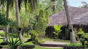 A tropical garden with a thatched-roof building, surrounded by lush greenery and palm trees. - Ravintsara Wellness Hotel (Nosy Be)