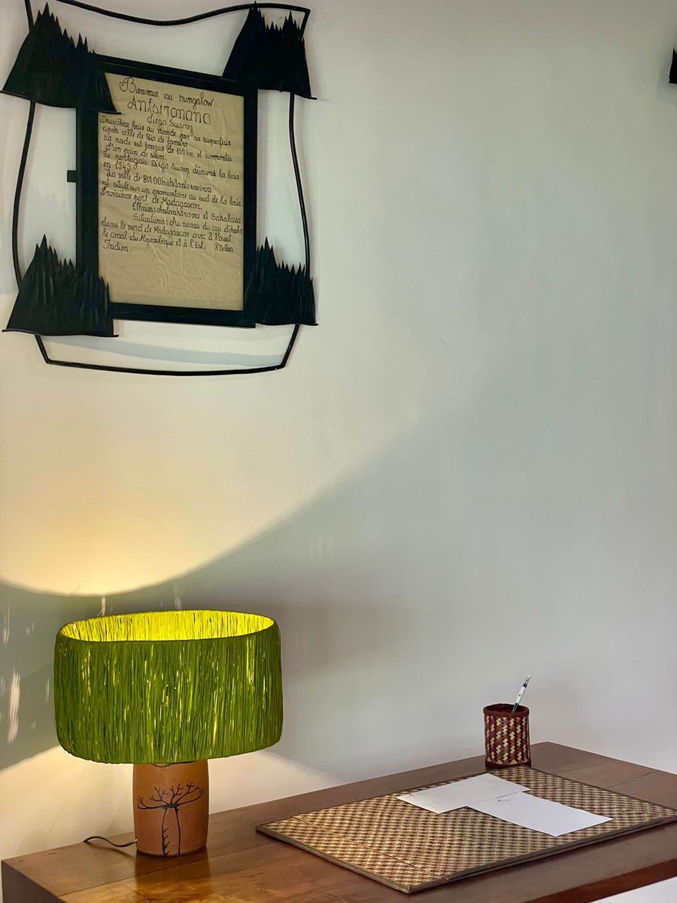 A room with a lamp on a wooden table, a framed document on the wall, and a small decorative item on the table.