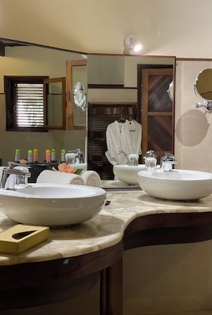 A bathroom with two sinks, a mirror, and a window with blinds. - Ravintsara Wellness Hotel (Nosy Be)