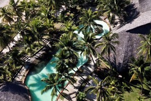 Vista aérea de un complejo turístico con piscina rodeada de palmeras y una terraza de madera.