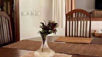 A dining table with a clear glass vase containing a plant, set on a brown placemat.