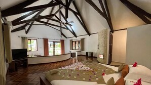 A spacious bedroom with a large bed, wooden beams, and a television. - Ravintsara Wellness Hotel (Nosy Be)