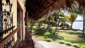 A covered outdoor area with a wooden deck, a thatched roof, and a view of a body of water.