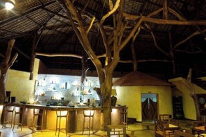 Un área de bar al aire libre con diseño rústico, que presenta un techo de paja y estructuras de madera.