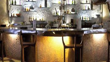 A bar with a rustic stone wall, shelves with bottles, and bar stools.
