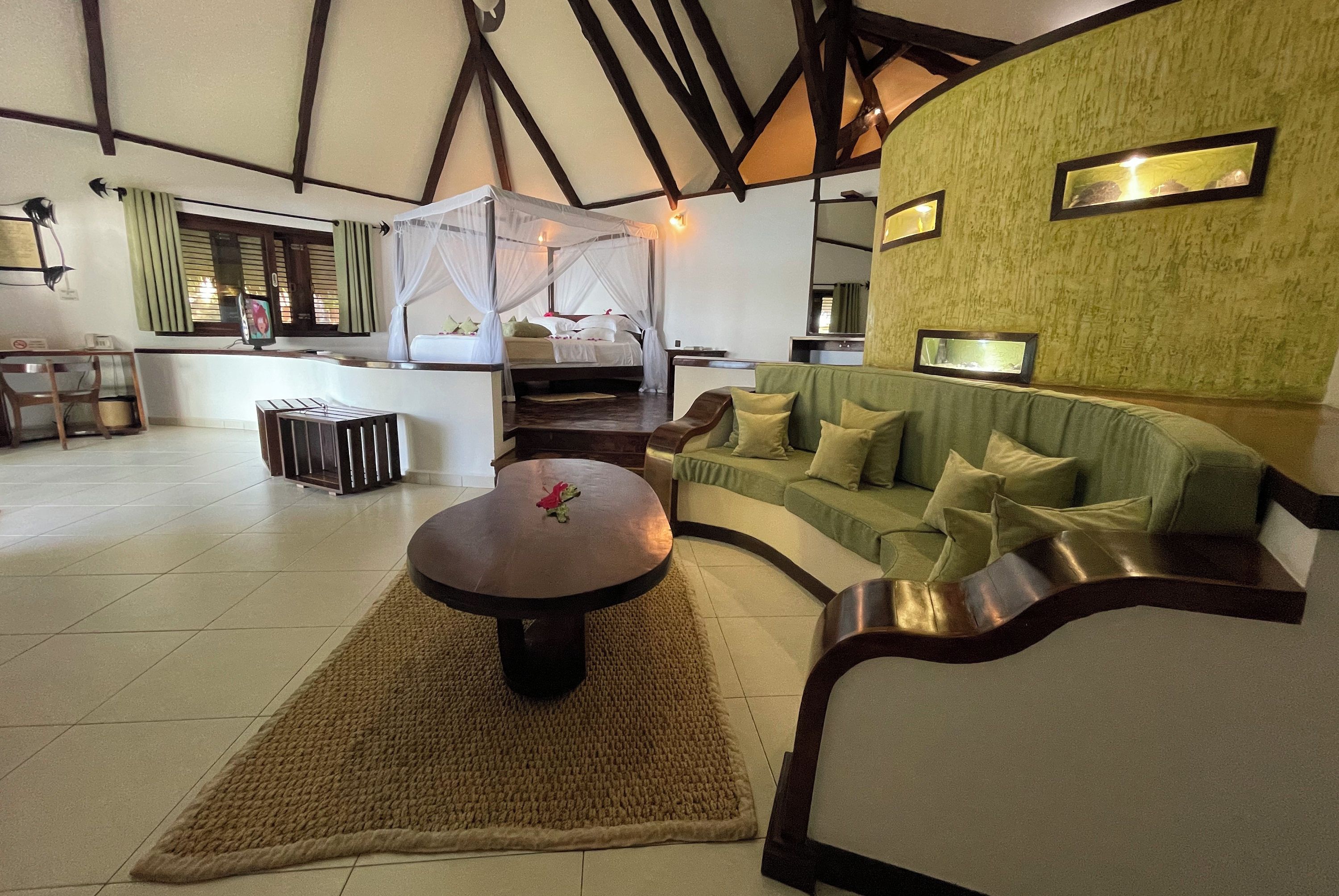 A spacious room with a large bed, a green sofa, a round table, and a dining area.