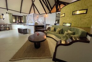A spacious room with a large bed, a green sofa, a round table, and a dining area. - Ravintsara Wellness Hotel (Nosy Be)