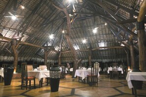 An indoor dining area with thatched roofs and wooden beams, tables set with white tablecloths, and large vases. - Ravintsara Wellness Hotel (Nosy Be)