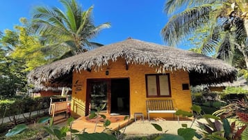 A small, single-story building with a thatched roof, surrounded by lush greenery and palm trees.