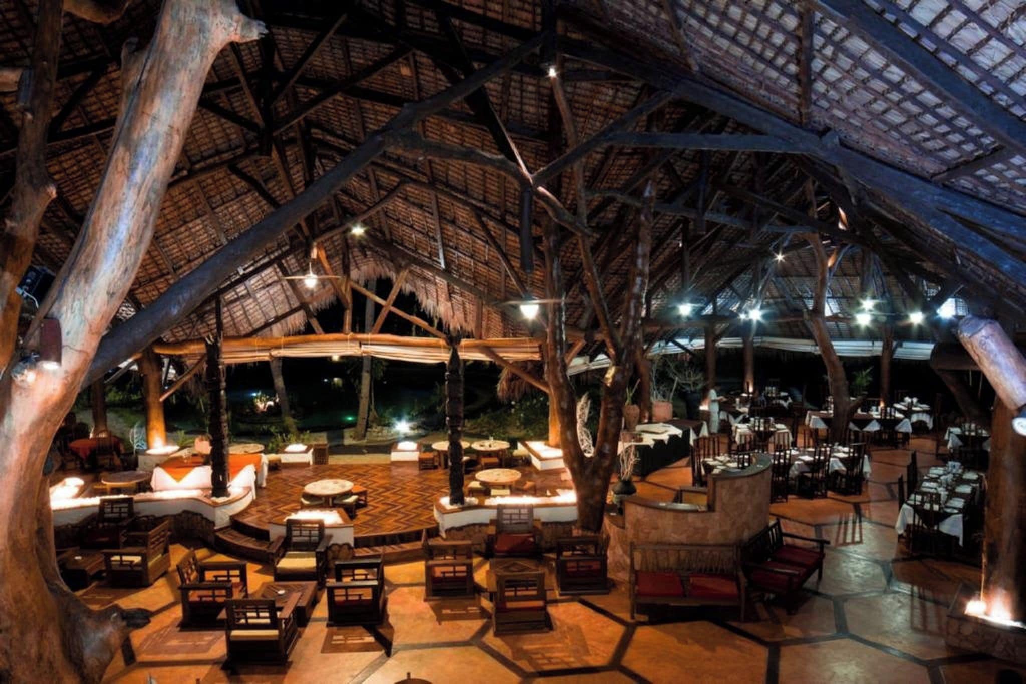 An outdoor dining area with thatched roof, wooden furniture, and ambient lighting.