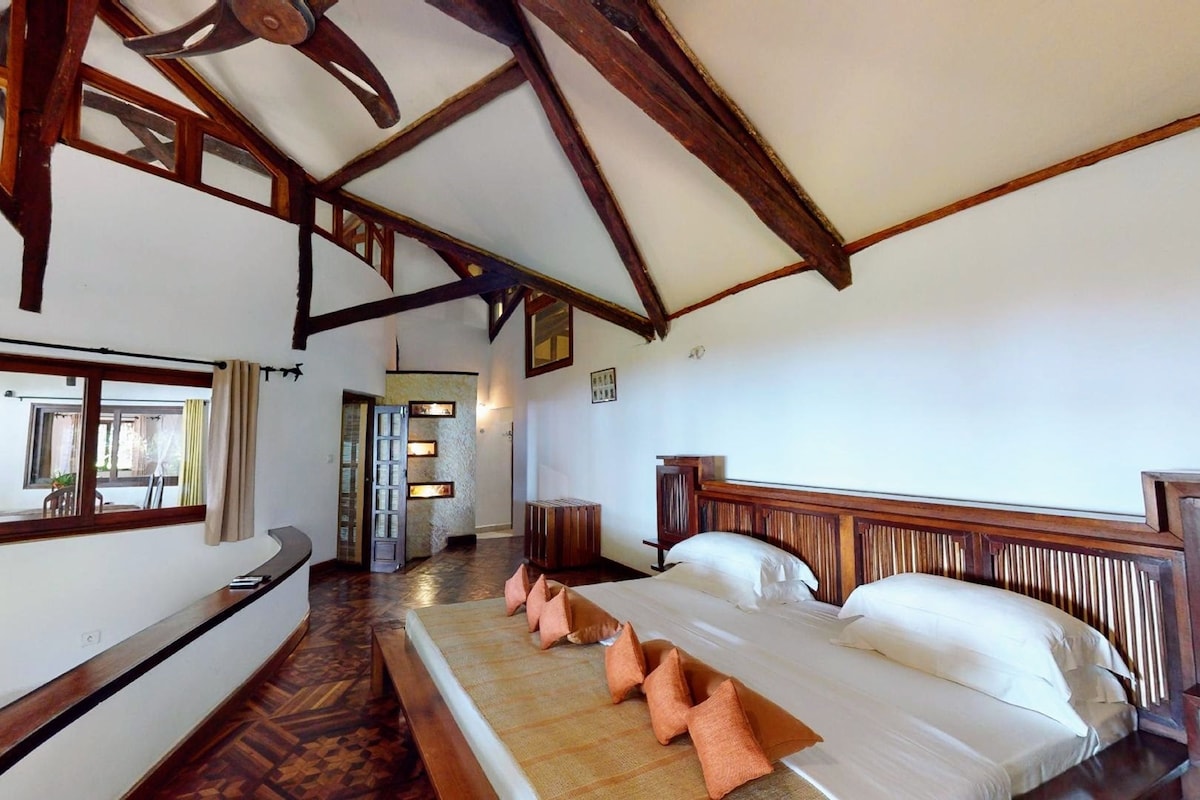 A room with a large bed, wooden beams, a window with curtains, and a view of the outside.