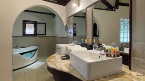 A modern bathroom with a large mirror, two sinks, a bathtub, and a vanity with toiletries. - Ravintsara Wellness Hotel (Nosy Be)