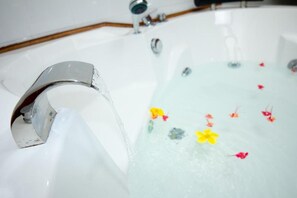 A bathtub with a chrome faucet and floral decorations in the water. - Ravintsara Wellness Hotel (Nosy Be)