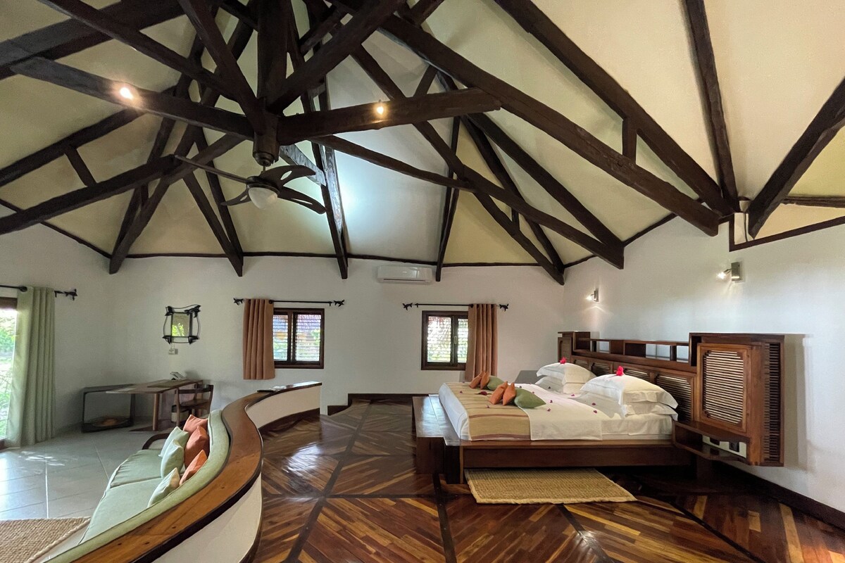 A bedroom with a wooden ceiling, a bed with white linens, and a wooden bench.