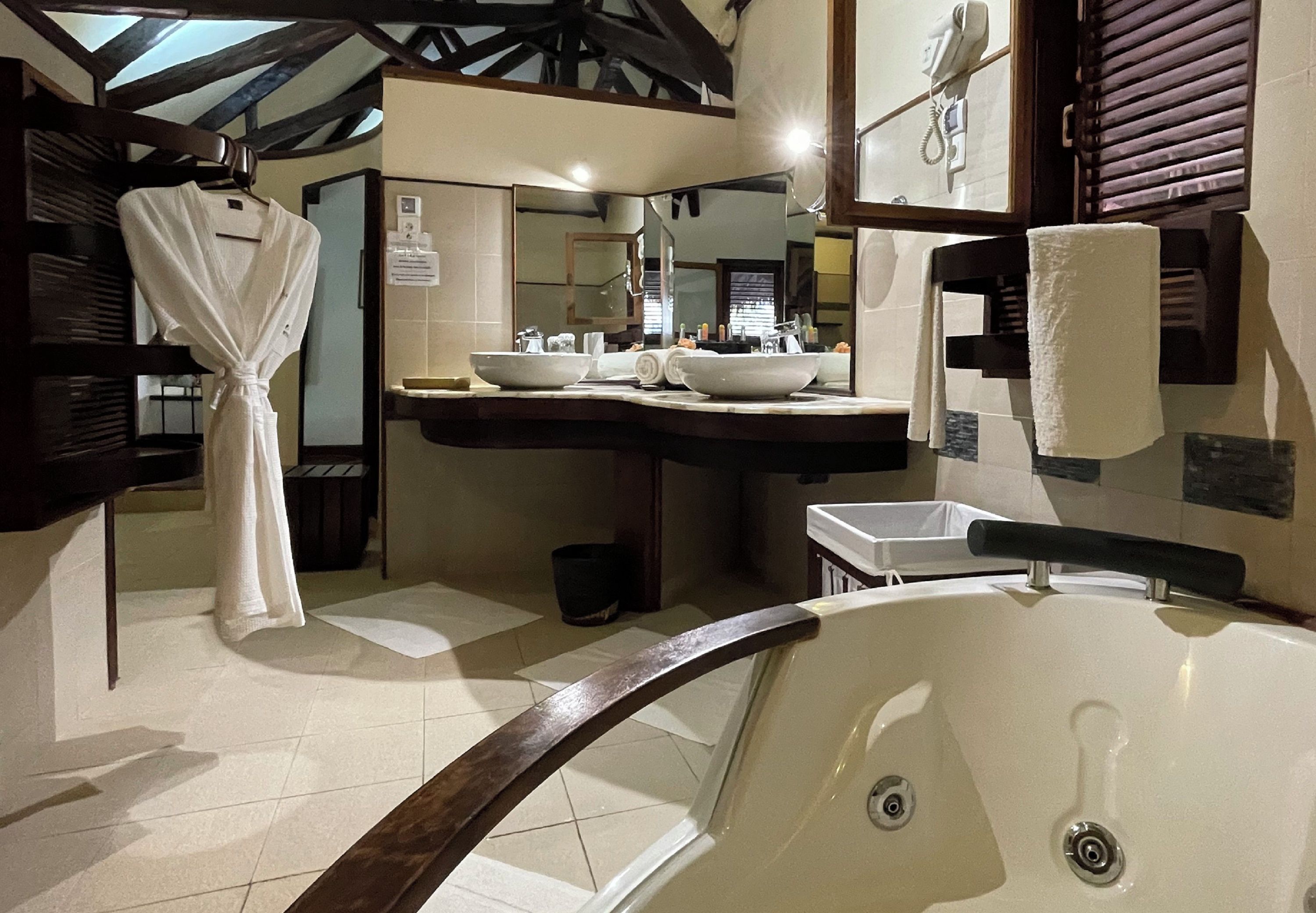A bathroom with a large bathtub, two sinks, a robe hanging, and a mirror above the sink.