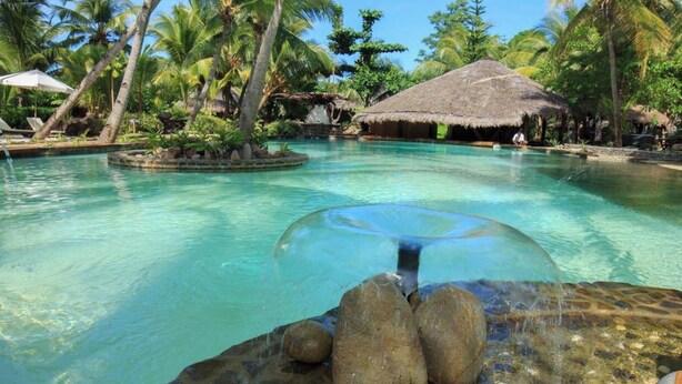 A clear pool with a glass dome, surrounded by palm trees and a thatched-roof hut. - Ravintsara Wellness Hotel (Nosy Be)