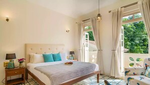 Un dormitorio con una cama grande, una mesita de noche, una silla y vistas al exterior con zonas verdes.