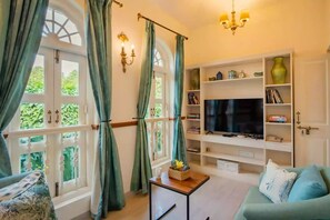 A living room with a TV, bookshelf, and a window with curtains. - Elivaas Monforte Ayada - Luxury Villa In Goa (Assagao)