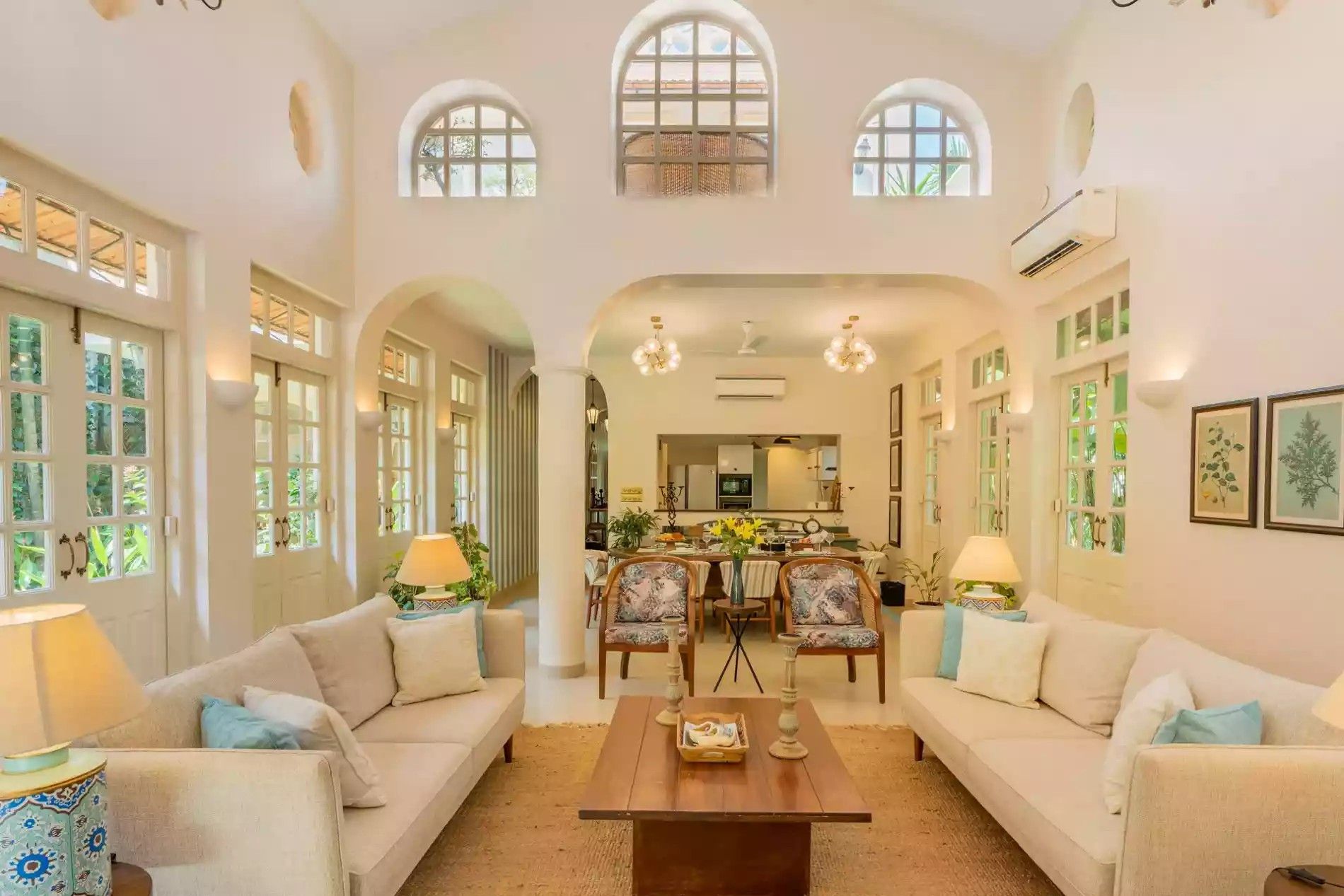 A spacious living room with high ceilings, large arched windows, and a central coffee table.