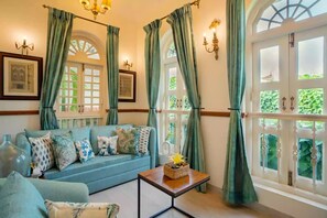 A cozy living room with a blue sofa, a small wooden table, and green curtains. - Elivaas Monforte Ayada - Luxury Villa In Goa (Assagao)