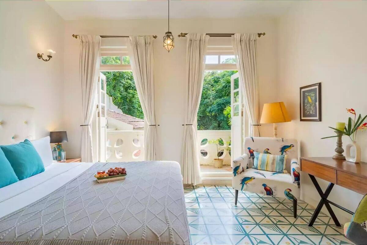 Un dormitorio con cama, escritorio, silla, lámpara y vista a zonas verdes.