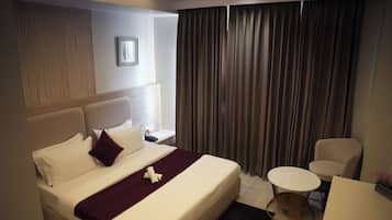 A hotel room with a large bed, a small round table, a chair, and a window with curtains.