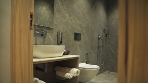 A modern bathroom with a marble wall, a white sink, a toilet, and a shower area. - Tr Hotels (Ambala)