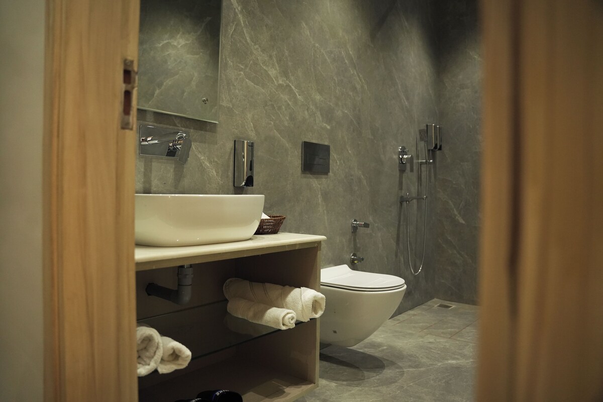 A modern bathroom with a marble wall, a white sink, a toilet, and a shower area.
