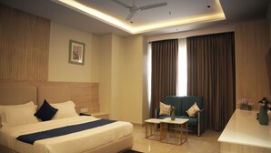 A hotel room with a bed, a desk, a chair, a ceiling fan, and a window with curtains. - Tr Hotels (Ambala)