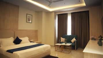 A hotel room with a bed, a desk, a chair, a ceiling fan, and a window with curtains.