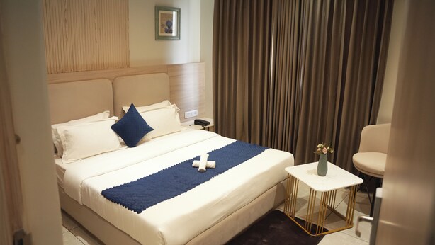 A hotel room with a bed, a small table with a vase, and a chair. - Tr Hotels (Ambala)