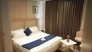 A hotel room with a bed, a small table with a vase, and a chair.