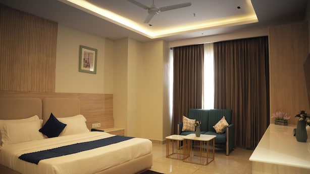 A hotel room with a bed, a desk, a chair, a ceiling fan, and a window with curtains. - Tr Hotels (Ambala)