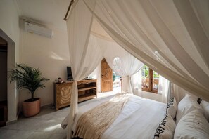 Un dormitorio con cama a dosel, una planta en maceta, un armario de madera y una ventana con vistas a zonas verdes.