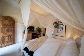 A bedroom with a canopy bed, a wooden door, a desk with a computer, and a plant. - Casa Coco (Lembongan Island)