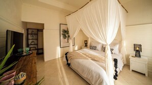 A bedroom with a four-poster bed, a bedside table, a nightstand, and a wall-mounted TV. - Casa Coco (Lembongan Island)