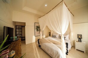 A bedroom with a four-poster bed, a bedside table, a nightstand, and a wall-mounted TV. - Casa Coco (Lembongan Island)