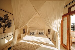 A bedroom with a canopy bed, a framed picture on the wall, and a wooden door. - Casa Coco (Lembongan Island)