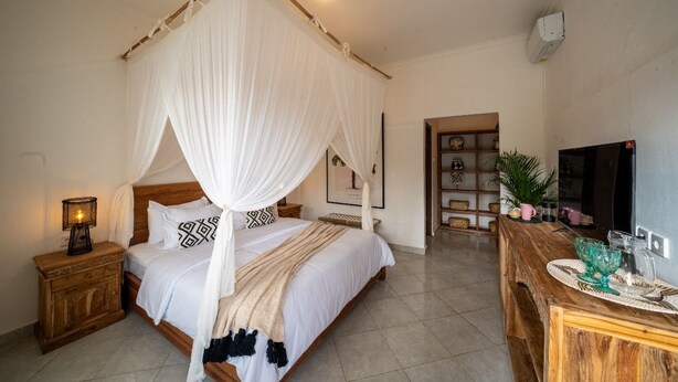 Une chambre à coucher avec un lit à baldaquin, une table de chevet avec une lampe, une commode en bois et un téléviseur.