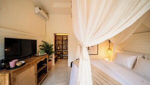 A bedroom with a TV, wooden cabinet, potted plant, and a bed with white bedding. - Casa Coco (Lembongan Island)