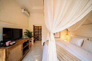 A bedroom with a TV, wooden cabinet, potted plant, and a bed with white bedding. - Casa Coco (Lembongan Island)