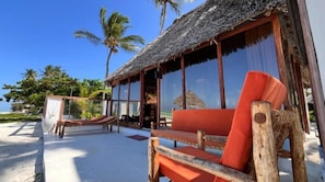A beachside hut with a thatched roof, wooden furniture, and large windows overlooking the ocean. - Tiki Beach Club & Resort (Paje)