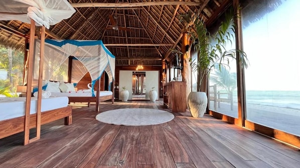 A wooden deck with a bed, a round rug, and a view of the ocean. - Tiki Beach Club & Resort (Paje)