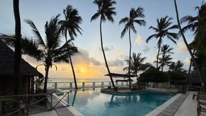 A pool area with a sunset view, surrounded by palm trees and a thatched-roof structure. - Tiki Beach Club & Resort (Paje)