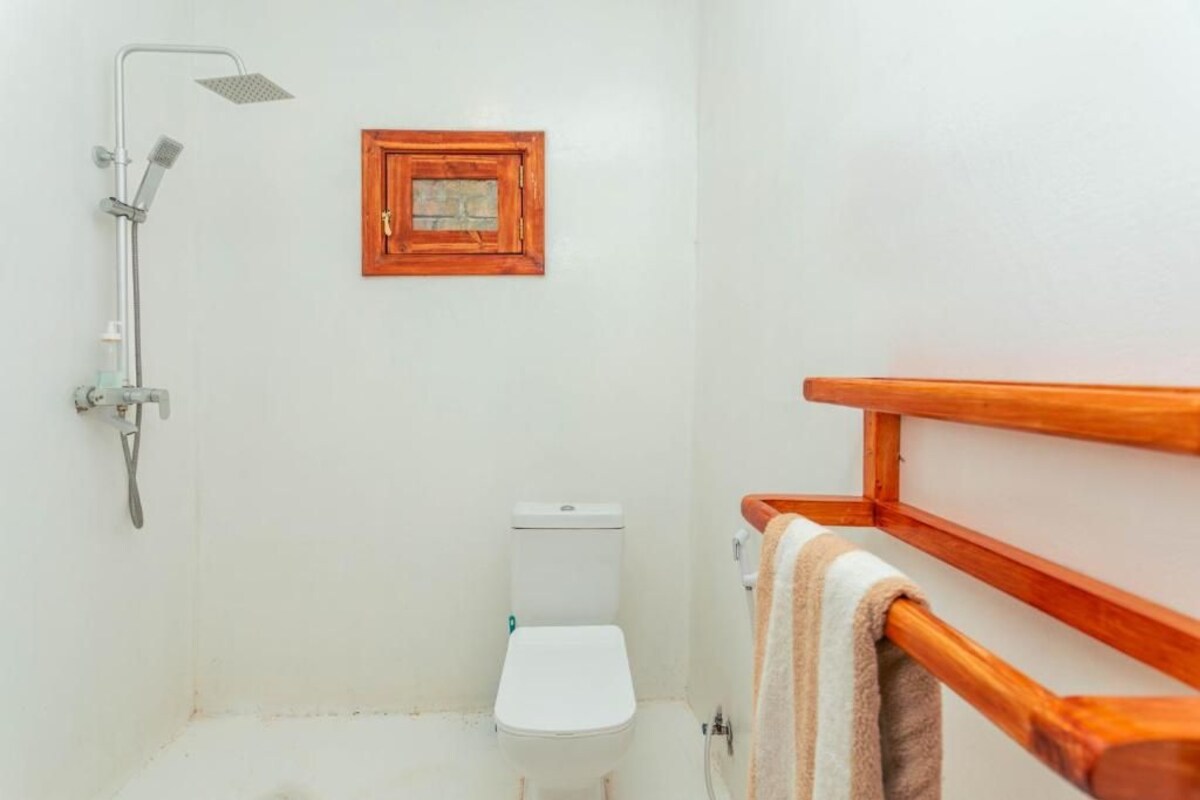 A small, compact bathroom with a shower, toilet, and a wooden-framed picture on the wall.